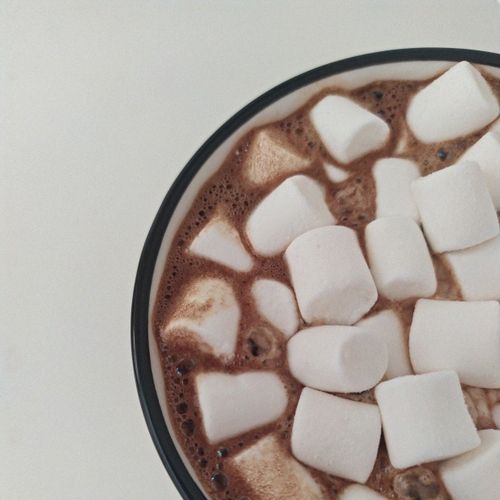 A top view of a steaming cup of hot chocolate topped with marshmallows on a white background.