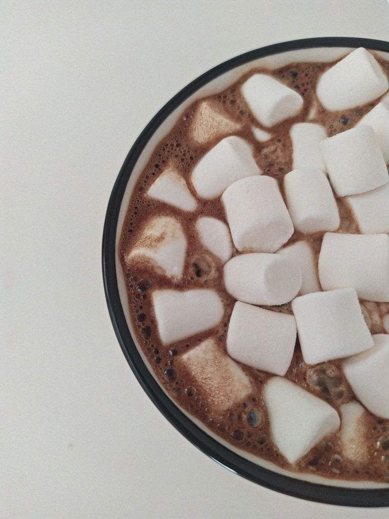 A top view of a steaming cup of hot chocolate topped with marshmallows on a white background.
