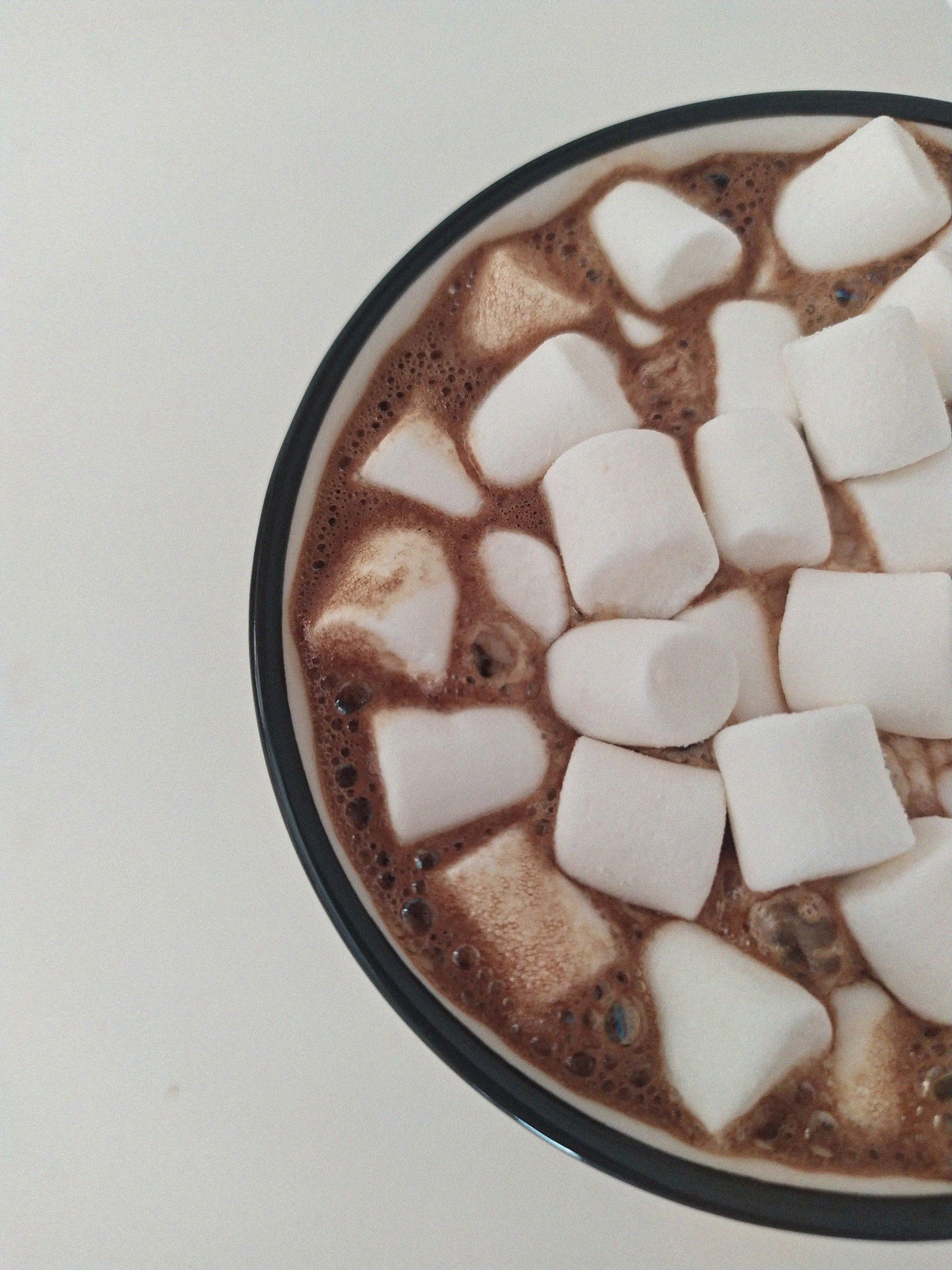 A top view of a steaming cup of hot chocolate topped with marshmallows on a white background.