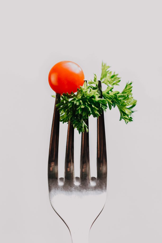 Close-up of a cherry tomato and fresh parsley on a fork against a white background.