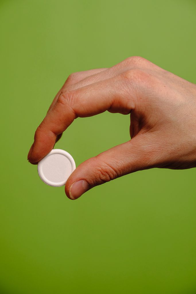 Close-up of a hand holding a white pill with a green background, highlighting medication.