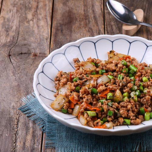 Delicious Asian stir-fry with minced meat and veggies in a white bowl on wooden table.