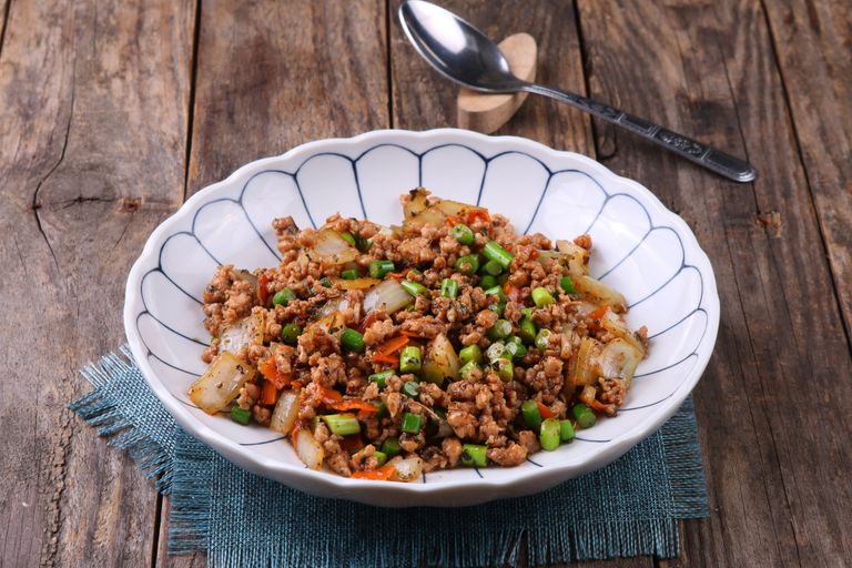 Delicious Asian stir-fry with minced meat and veggies in a white bowl on wooden table.