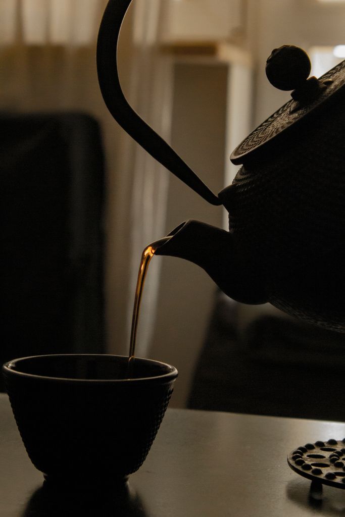 Elegantly pouring tea from a vintage kettle into a teacup in a moody, dimly lit setting.