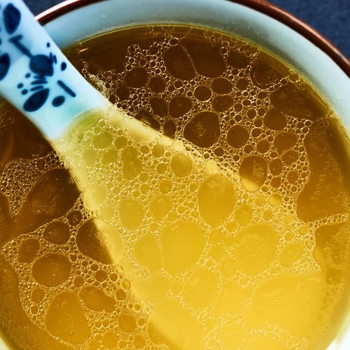 Warm, comforting chicken broth in a bowl with decorative spoon close-up.